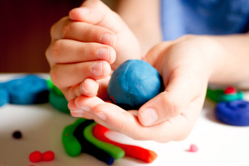 Child hands molding modeling clay or plasticine on white table