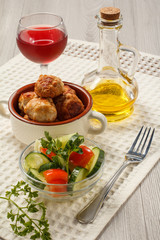 Fried meat cutlets in ceramic soup bowl, glass of wine, bottle with sunflower oil and salad of fresh cucumbers and tomatoes in glass bowl on white kitchen towel