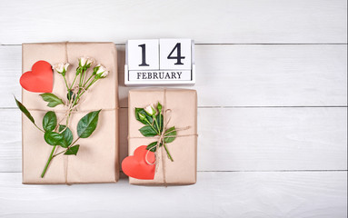 Top view of block calendar with february 14 and gift boxes wrapped in kraft with fresh roses and red hearts on wooden table, copy space. Sale, shopping. Greeting card for Valentines Day, flat lay