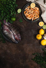 fresh raw fish, shrimp, herbs with lemons and tablecloth on dark table top