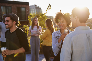 Happy friends at a rooftop party backlit by sunlight - obrazy, fototapety, plakaty