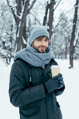 Fototapeta na wymiar portrait of handsome young man with coffee to go in hands in snowy park