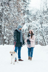Fototapeta na wymiar young couple with dog walking in winter snowy park