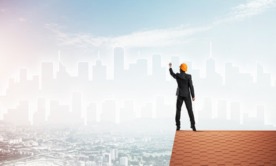Man architect draw silhouette of modern city on blue sky. Mixed media