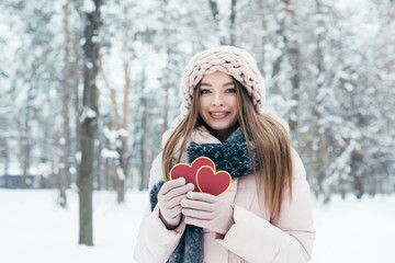 portrait of beautiful young woman with hearts in hands looking at camera in snowy park