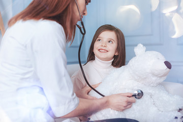 Good mood. Little patient keeping smile on her face and holding her bear on the knees while sitting...