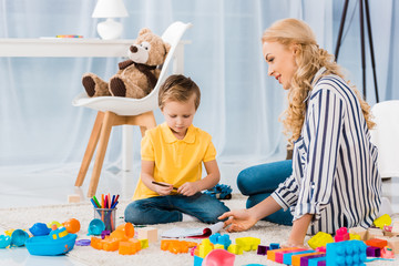 Naklejka premium young mother helping son while drawing picture together at home
