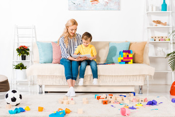 young mother and son drawing picture together while resting on sofa at home