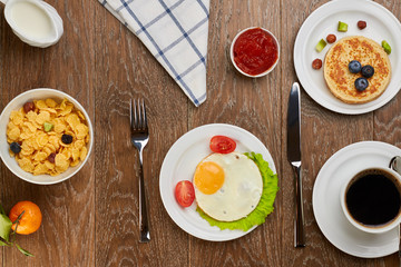 top view of fried eggs with tomatoes and lettuce,  pancake with blueberries on plate, and cornflakes,