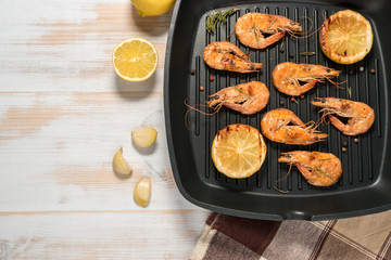 Grilled shrimps on a grill frying pan with lemon, paprika, spices and herbs. Wooden background.