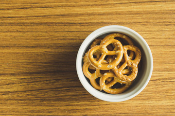 Mini pretzels in white bowl on the wooden table.