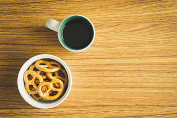 Mini pretzels in the bowl and black coffee on wooden background.