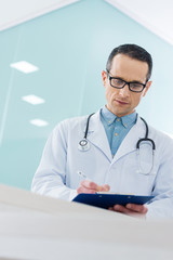 confident doctor in white coat with stethoscope writing diagnosis in hospital