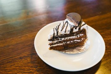 Chocolate cake in a white plate on wooden table.