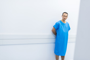 male patient in medical gown standing at wall in hospital