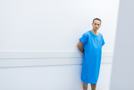 Male Patient In Medical Gown Standing At Wall In Hospital