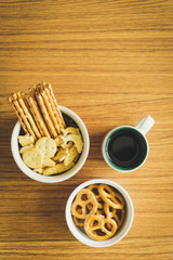 Mini pretzels in the bowl and black coffee on wooden background.
