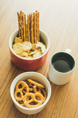 Mini pretzels in the bowl and black coffee on wooden background.