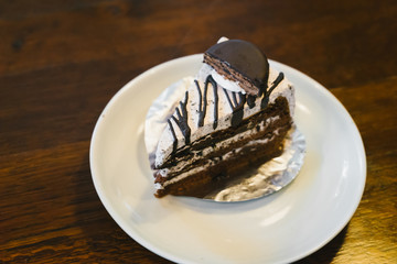 Chocolate cake in a white plate on wooden table.