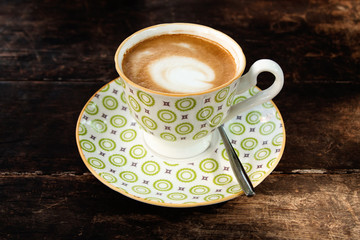 Hot cappuccino in a white-green cup on a wooden table in a cafe.