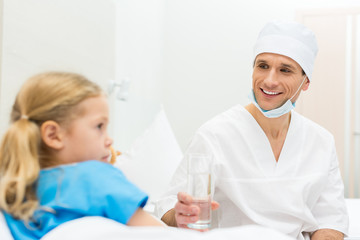 smiling doctor giving sick kid glass of water