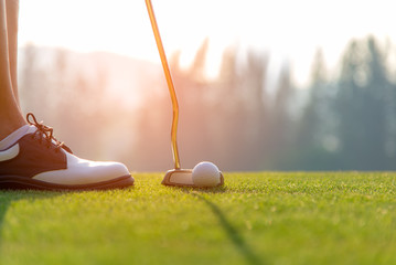 Golfer asian woman putting golf ball on the green golf on sun set evening time.  Healthy and...