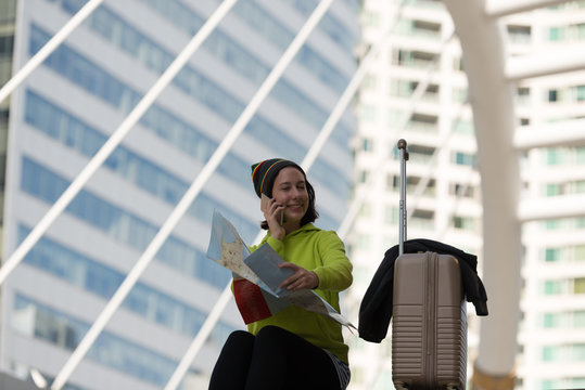 Happy traveler using a smartphone while sitting and hand of hold map with suitcase is waiting for transport, Travel concept.