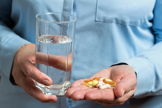 Woman take in the hand variety medication pills, yellow capsules of omega 3, glucosamine and calcium dietary supplements and glass with water in the other hand