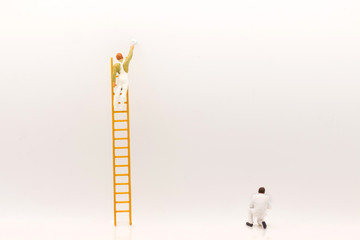 miniature people, mini figure with ladder and white paint in front of a wall and another one paint on bottom of wall.