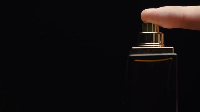Fragrance luxury bottle contents in dark spraying slow motion. Perfume bottle spray on black background. Spraying Cologne on a black background. lose up of handsome young business man using perfume or