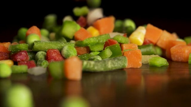 Chopped vegetables. Slices of red and green peppers, carrots, green beans, peas, onion, corn falling on black background. Slow Motion. Chopped vegetables fall on black background