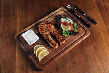Fototapeta na wymiar grilled salmon steak served on wooden board with lemon and lettuce