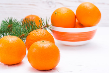 Ripe mandarins on a table and in a bowl and fir branches