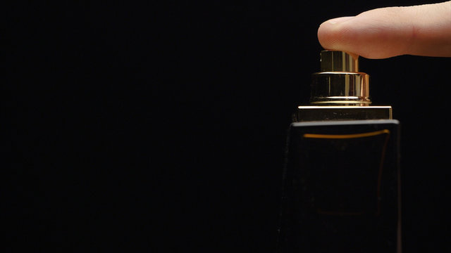 Fragrance luxury bottle contents in dark spraying slow motion. Perfume bottle spray on black background. Spraying Cologne on a black background. lose up of handsome young business man using perfume or