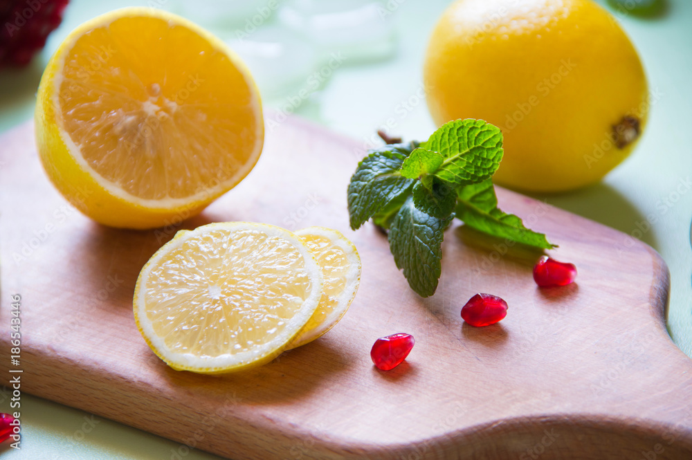 Wall mural Lemon with pomegranate and mint is cut on a wooden board