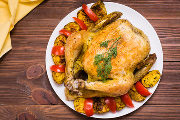 Baked whole chicken with a garnish of potatoes and tomatoes on a plate. Top view