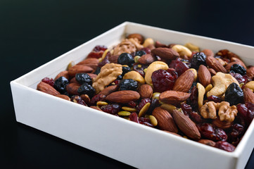 Many different nuts (almonds, cashews, walnuts), dried berries (blueberries, cranberries) in a white box on a black background. Antioxidant product. Healthy food.