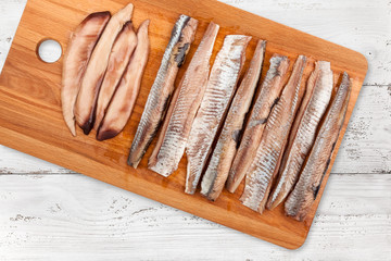Wooden cutting board with a herring fillet on light wooden background, top view