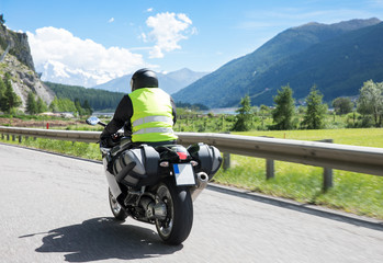 Motorradfahrer fährt mit seinem Motorrad auf kurvigen Straßen durch die Berge und einer...