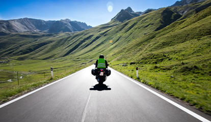 Motorradfahrer fährt mit seinem Motorrad auf kurvigen Straßen durch die Berge und einer wunderschöne Landschaft