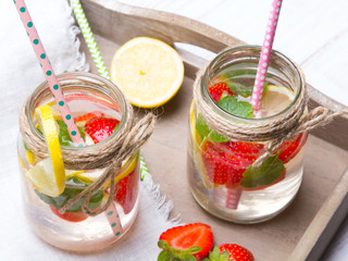 Mineral  water with fresh strawberries, lemon  and mint in jar on a white wooden background, copy space