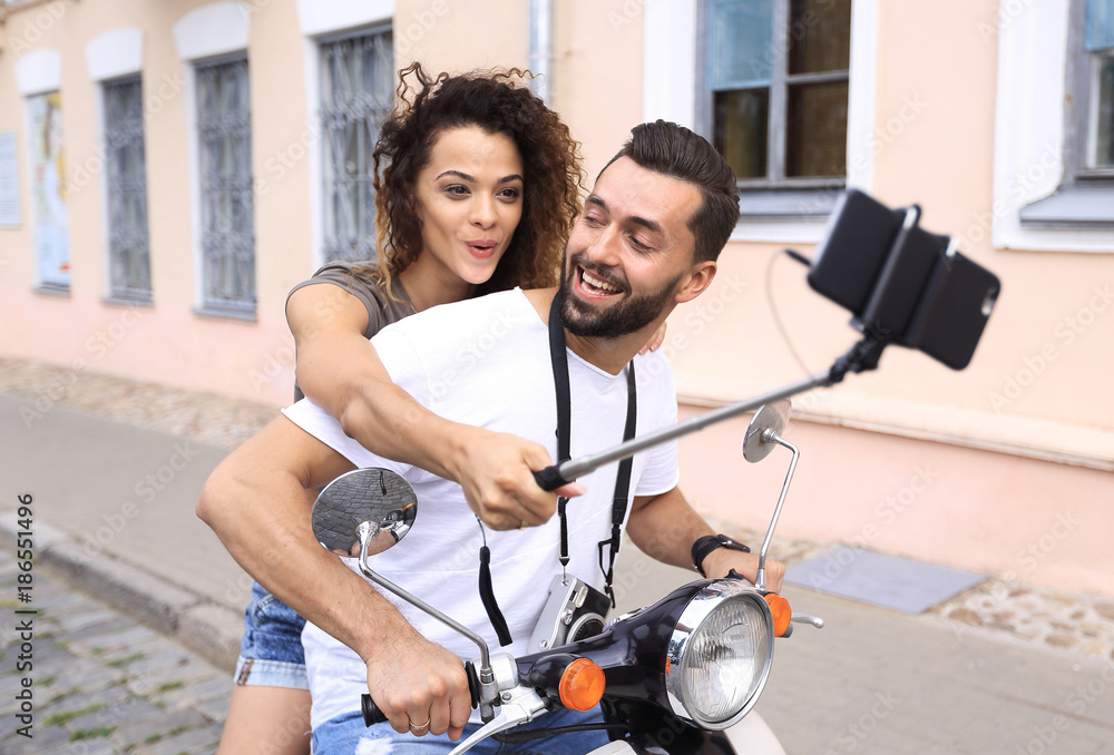 Wall mural Happy couple on scooter making selfie on smartphone outdoor