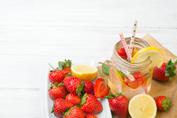 Mineral  water with fresh strawberries, lemon  and mint in jar on a white wooden background, copy space