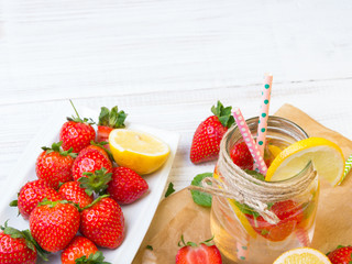 Mineral  water with fresh strawberries, lemon  and mint in jar on a white wooden background, copy space