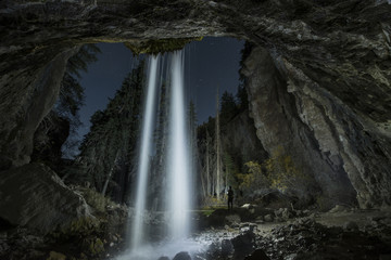 Rear view of silhouette man standing by waterfall in forest at night