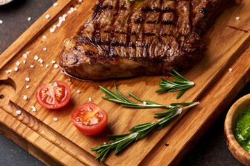 Grilled Black Angus Steak with tomatoes, garlic with rosemary on meat cutting board.