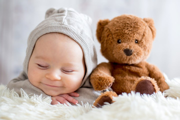 Sweet baby boy in bear overall, sleeping in bed with teddy bear