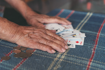 Active retirement, old people and seniors free time, selected focus on old women wrinkle hands having fun and playing cards game at home with some coins on right hand side