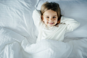 Top view of little girls while lying in white bed at home