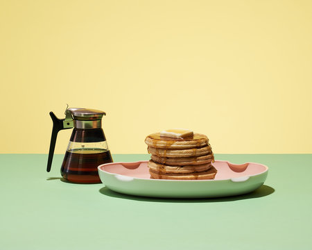 Pancake waffles and syrup served on a table against yellow background
